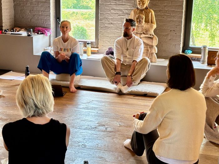 Sven zit vooraan op een meditatiekussen tijdens een live groepssessie, voor een houten boeddhabeeld.